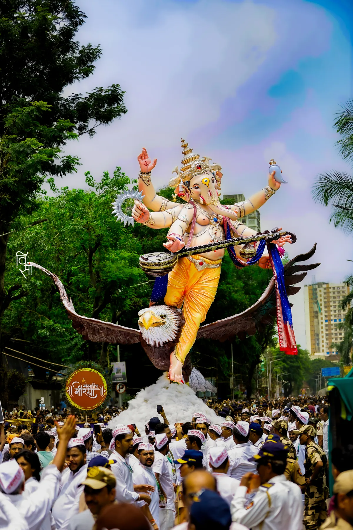 The 2026 murti above a street full of devotees in white caps during aagman