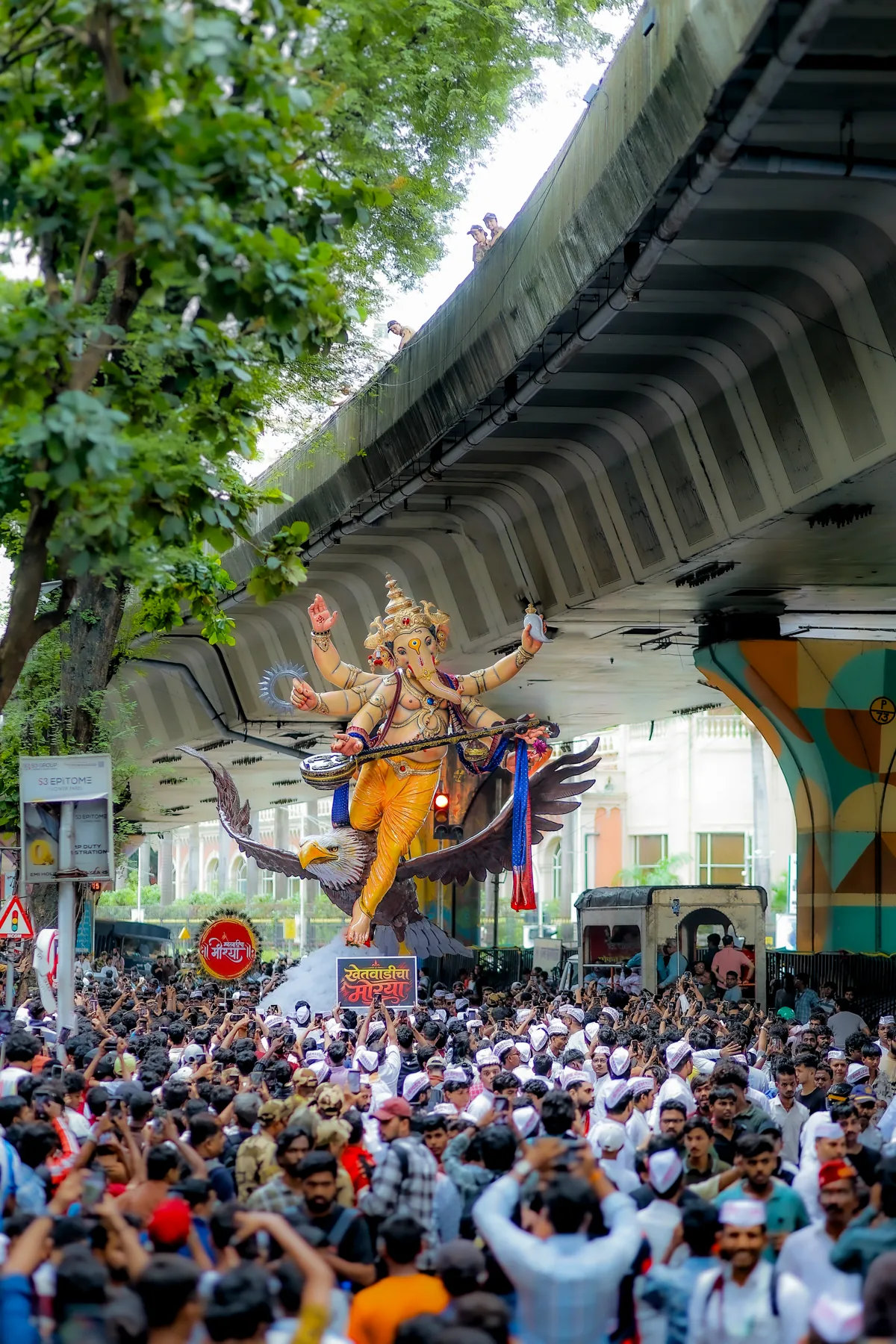 The murti passing under a flyover above a sea of devotees